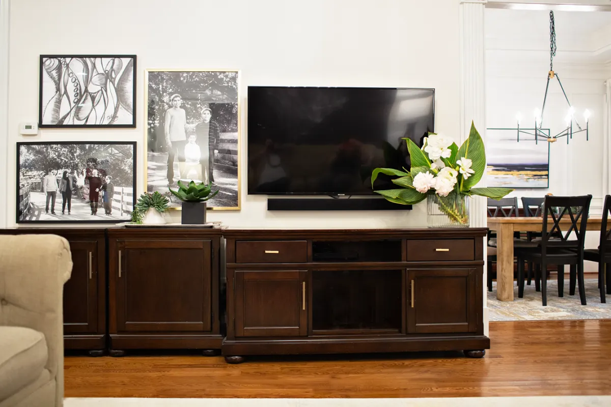 Dark wooden tv cabinet with a wall mounted tv, and 3 framed black and white photos.