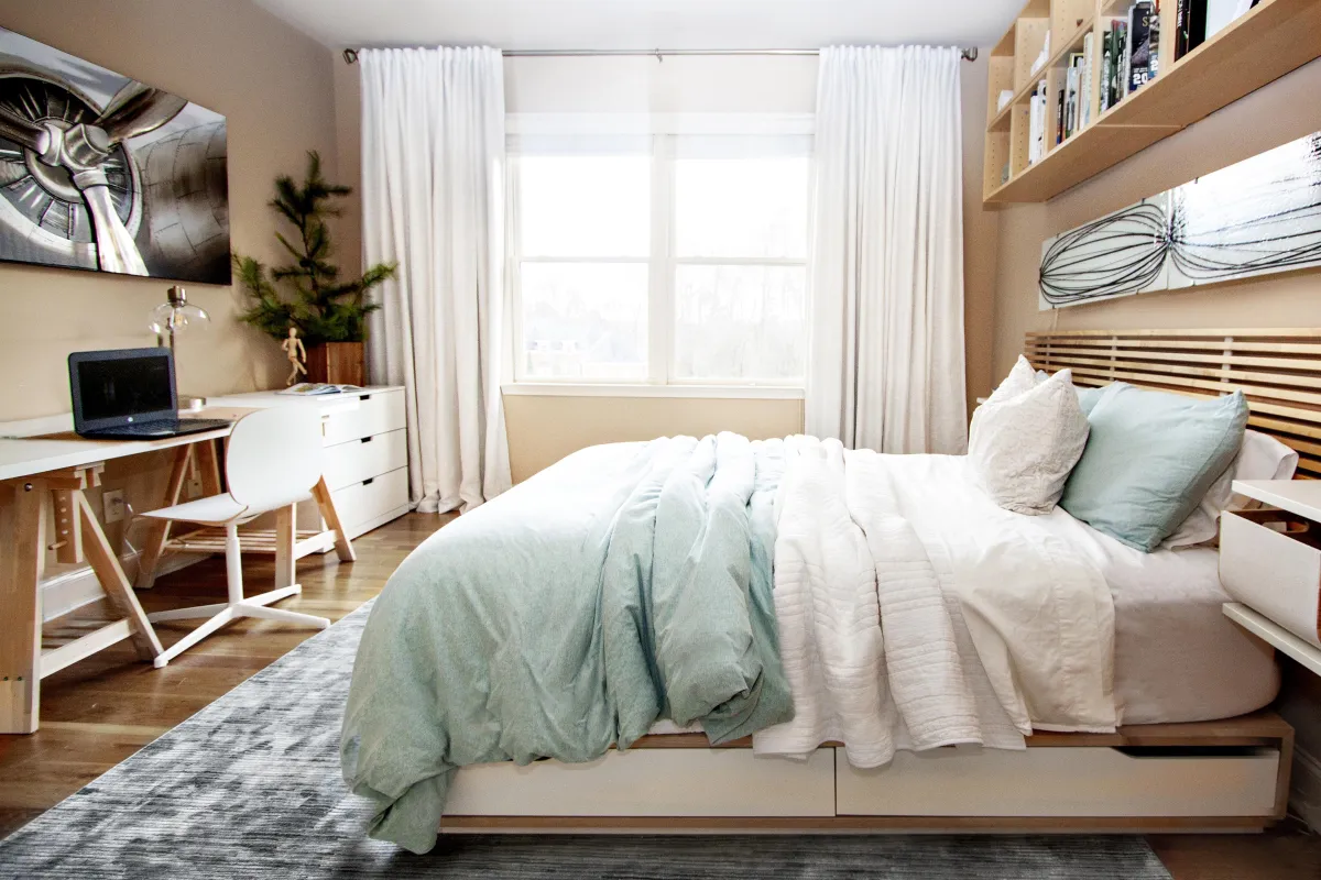 Cozy boys’ bedroom showcasing a full size bed with mint green bedding, a wooden desk, and white floor-to-ceiling curtains.