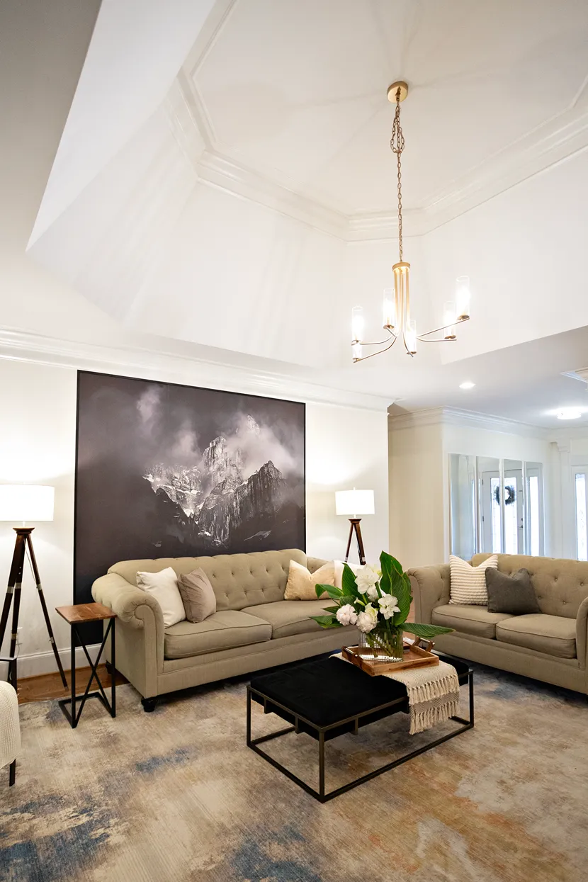 Traditional style white living room showcasing a light brown linen sofa and loveseat, recessed ceiling, and golden chandelier.