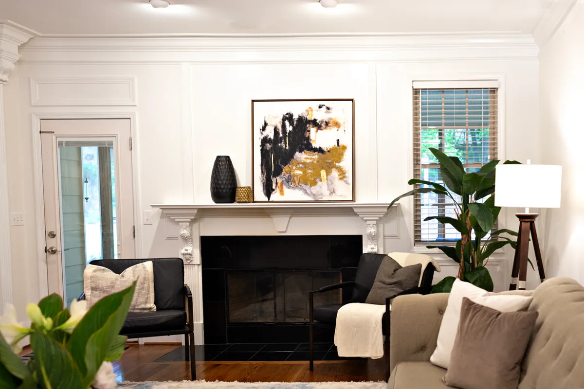 Earthy toned living room with fireplace, matching black armchairs, abstract painting, and a large floor plant.