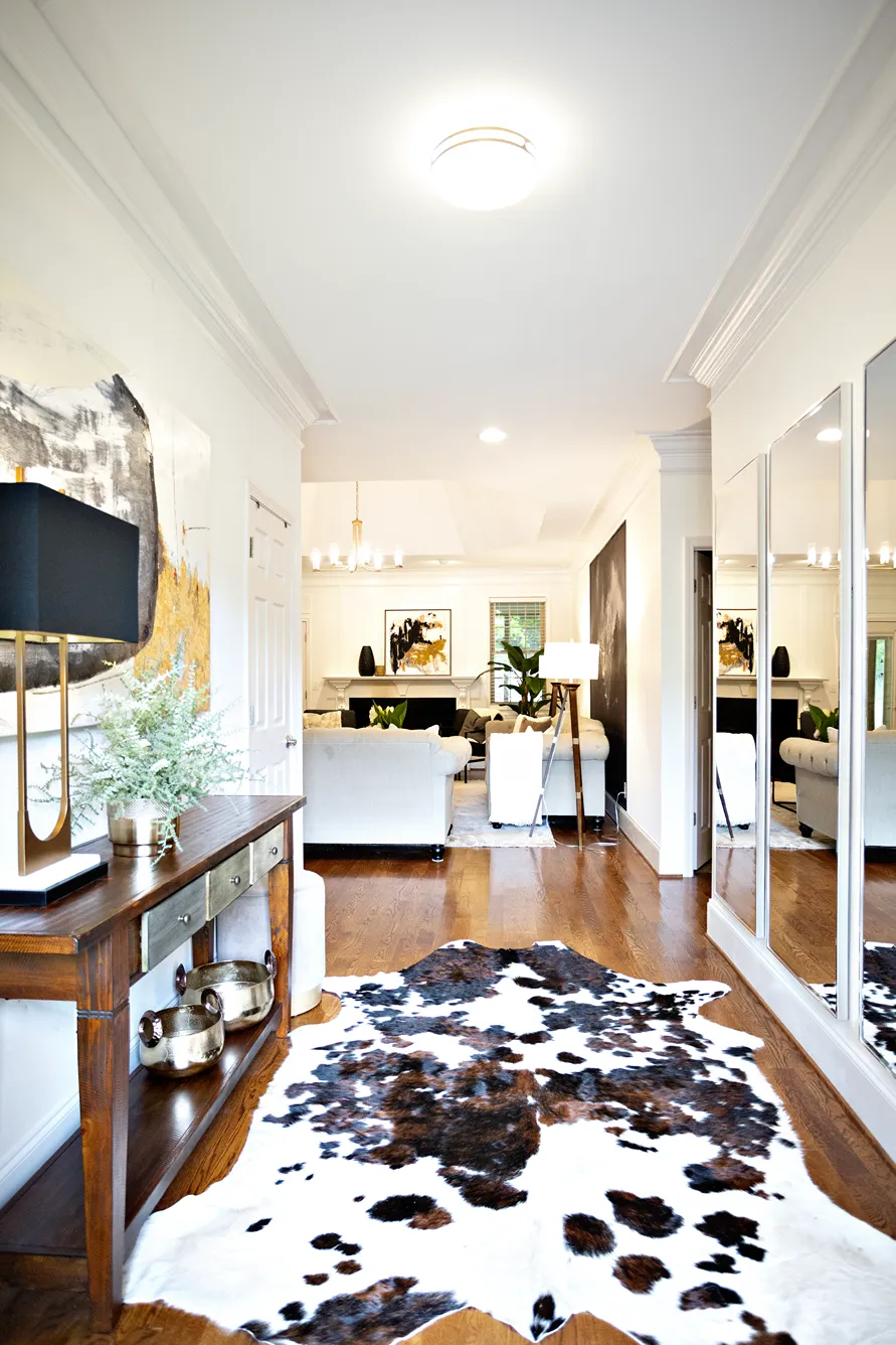 Welcoming entryway with a wooden console table, abstract painting, and a faux white and brown cowhide rug.