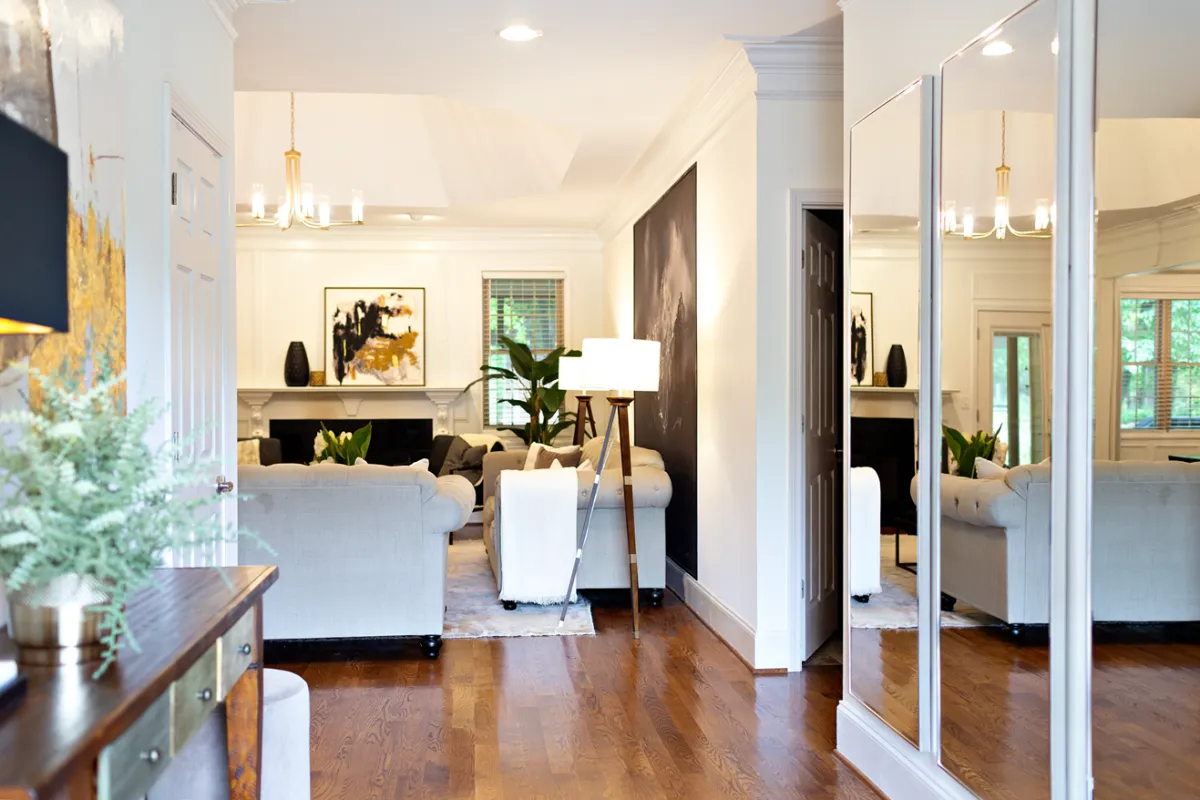 welcoming entryway featuring a dark wooden console table opposite 3 large rectangular mirrors, leading into a traditional living room.