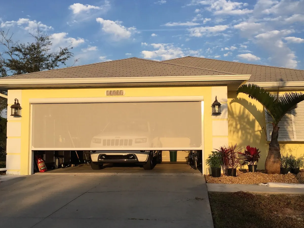 A double garage door with two FL Outdoor Motorized Screens mount on the outside of this spanish style home. 