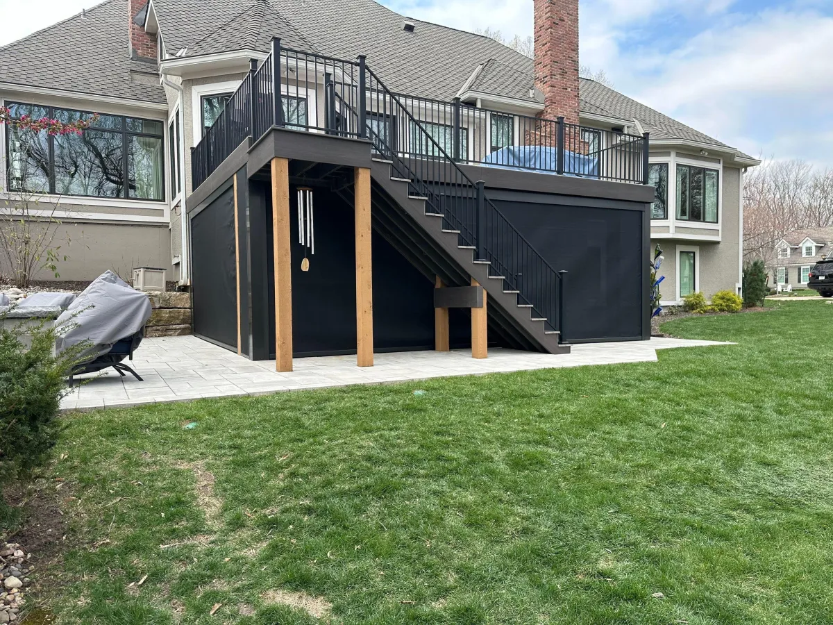 A luxurious backyard featuring a swimming pool with blue water, surrounded by a paved patio: An open patio cover overlooks the pool, connected to a modern house with large sliding doors and an outdoor seating area protected by retractable motorized screens.