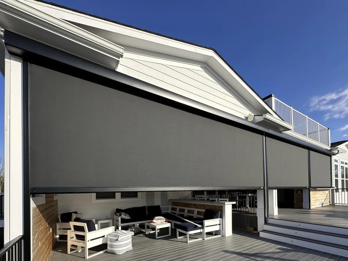 A modern outdoor seating area with large retractable insect screens, white wooden siding, and contemporary furniture under clear blue skies.