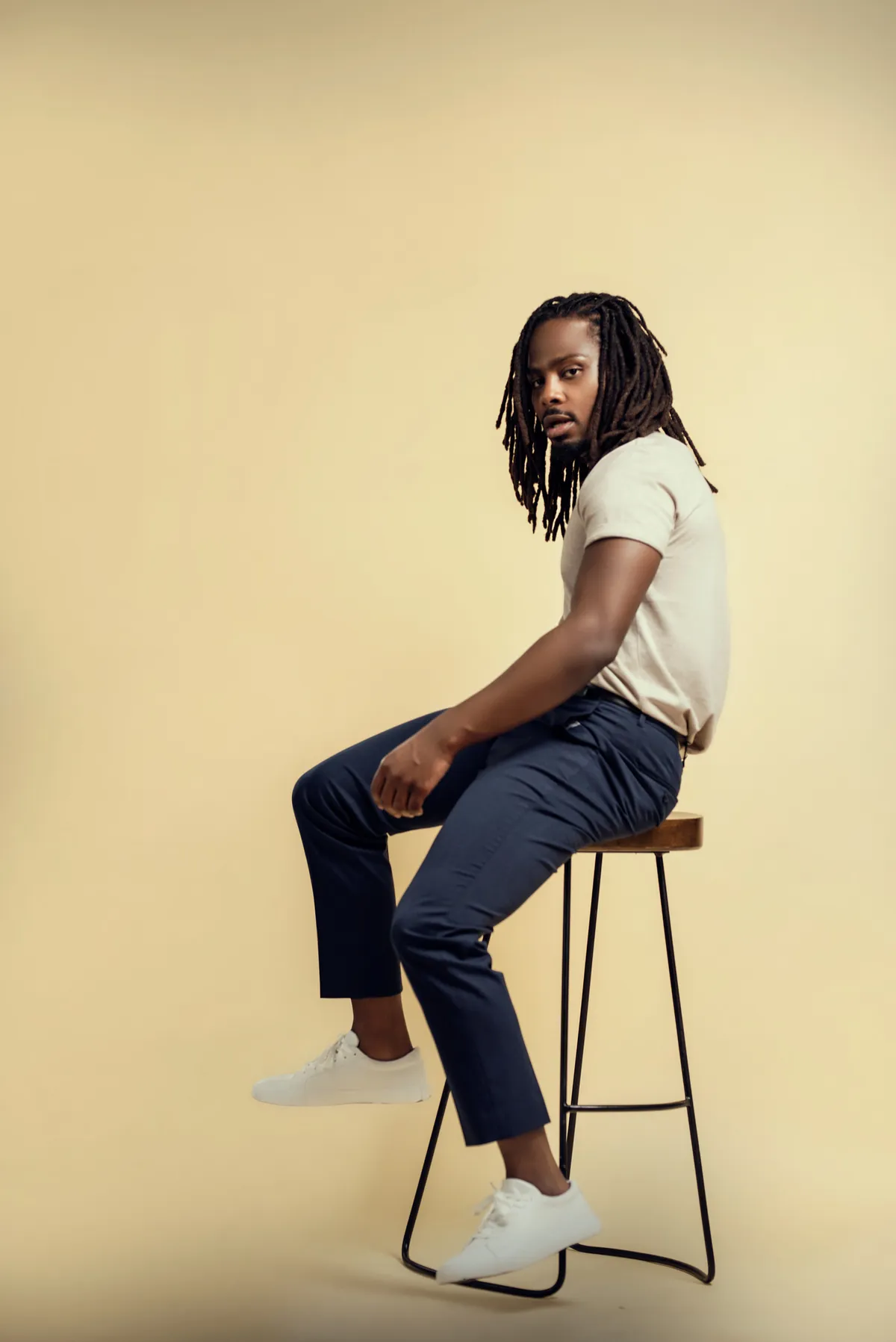 Full length portrait of a man seated on a stool on a warm backdrop