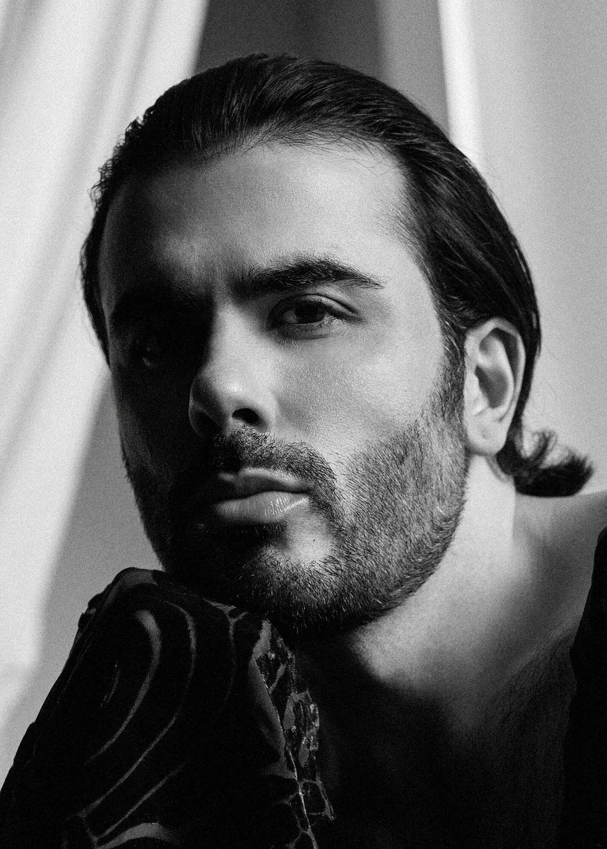 Black and white close portrait of a bearded man with slicked back hair, lit from one side
