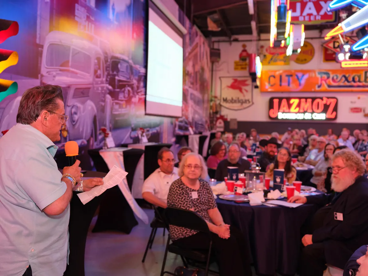 Speaker with a microphone addressing seated guests at a reunion dinner