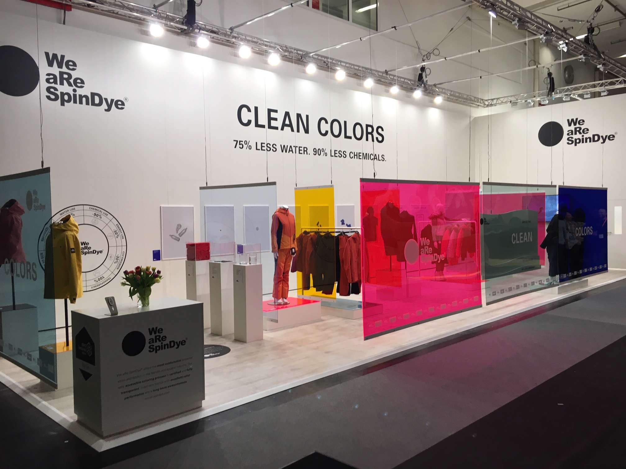 Promotional graphic for SpinDye Clean Colors featuring repeated branding with environmental impact statistics: "75% less water, 90% less chemicals." Highlights sustainable dyeing technology for eco-friendly textile manufacturing.