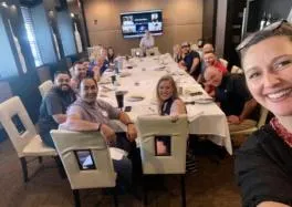 Team building dinner group photo: diverse group of professionals posing for a selfie at a corporate dinner event in a modern dining room