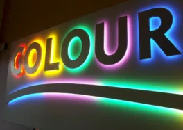 Vibrant multicolored illuminated 'COLOUR' sign with rainbow neon lighting at night.