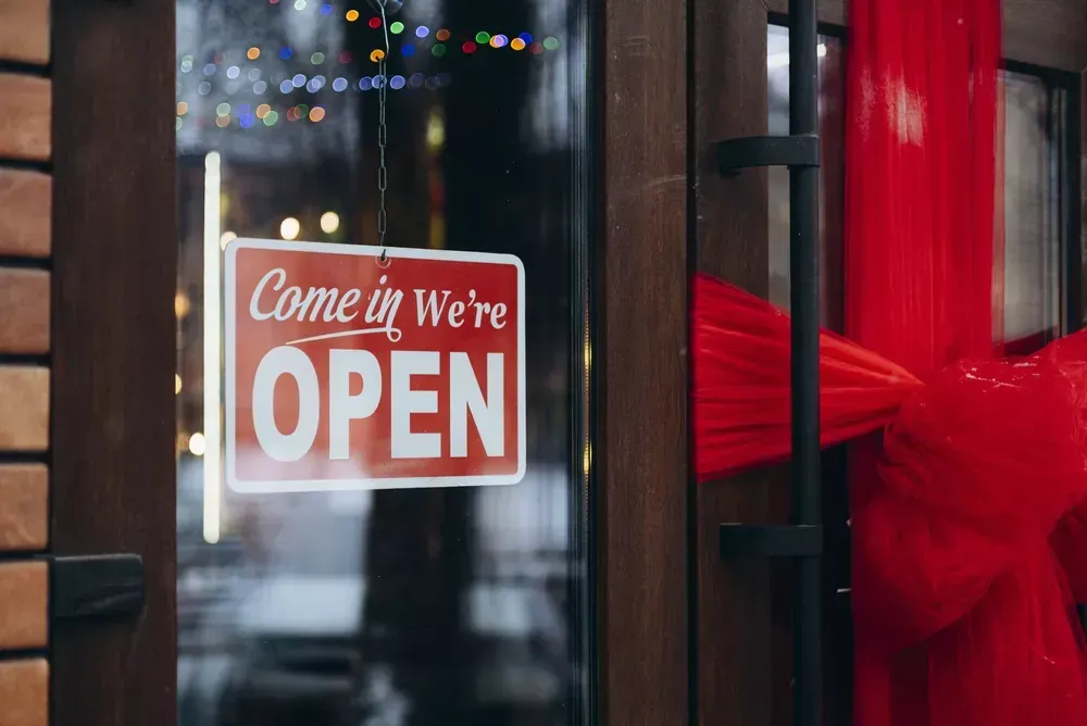 Open business door sign on a glass storefront entrance reading “Come in We’re Open,” used for retail door signage, storefront branding, and welcoming customers into a business location.
