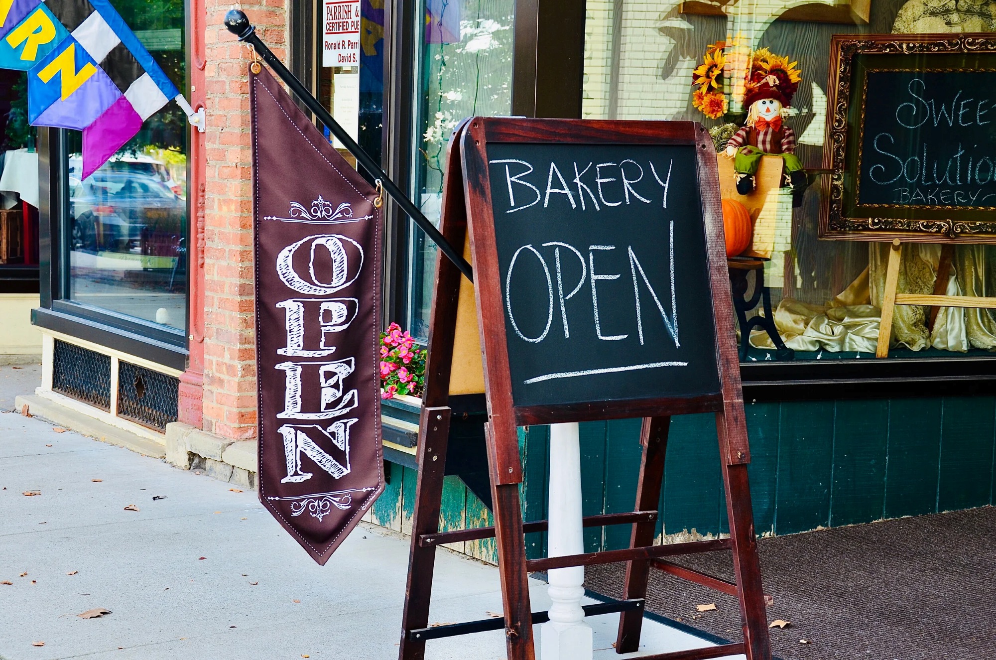Bakery storefront with sidewalk chalkboard sign reading “Bakery Open”