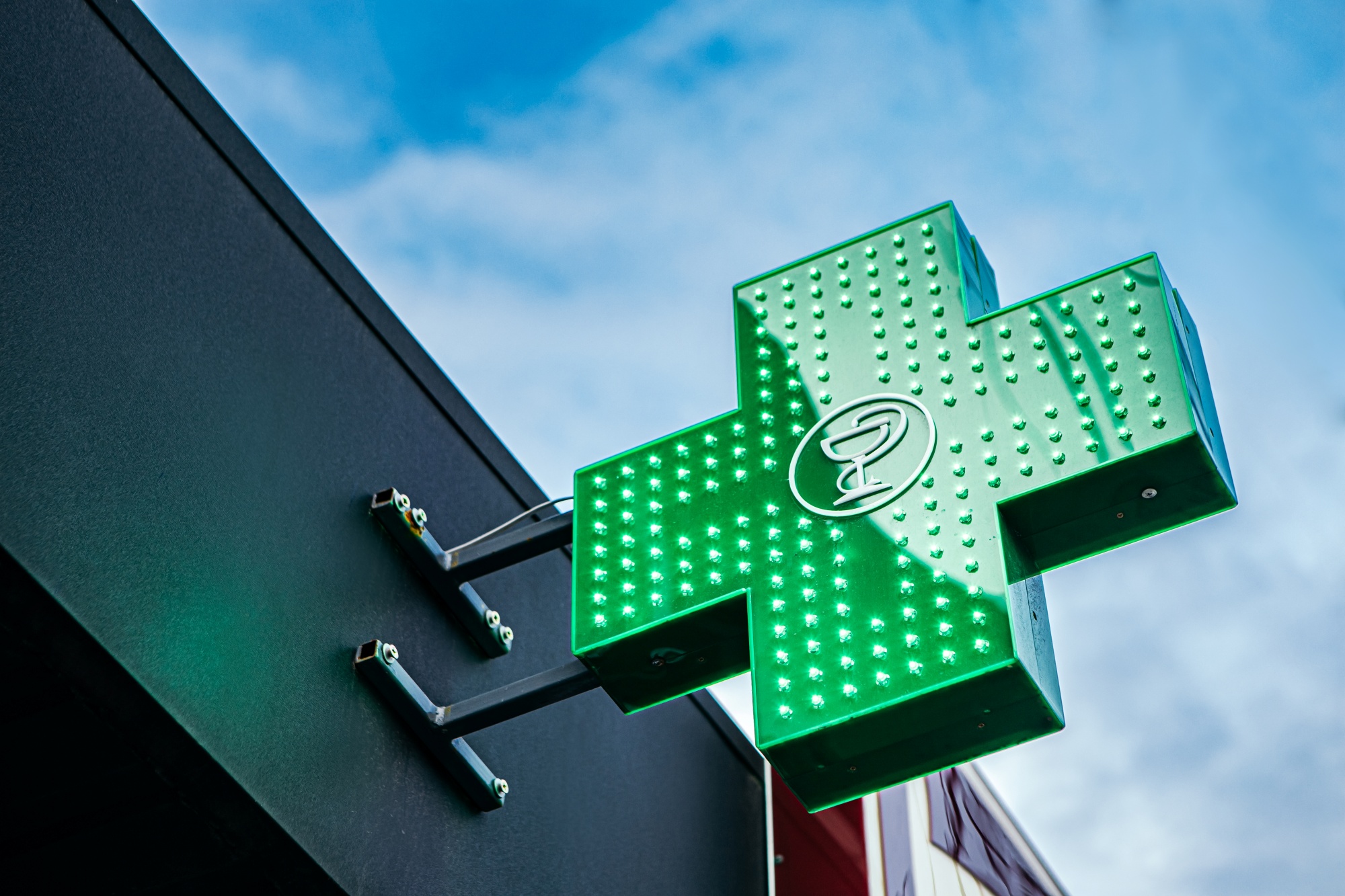 Illuminated green pharmacy cross sign mounted on building exterior