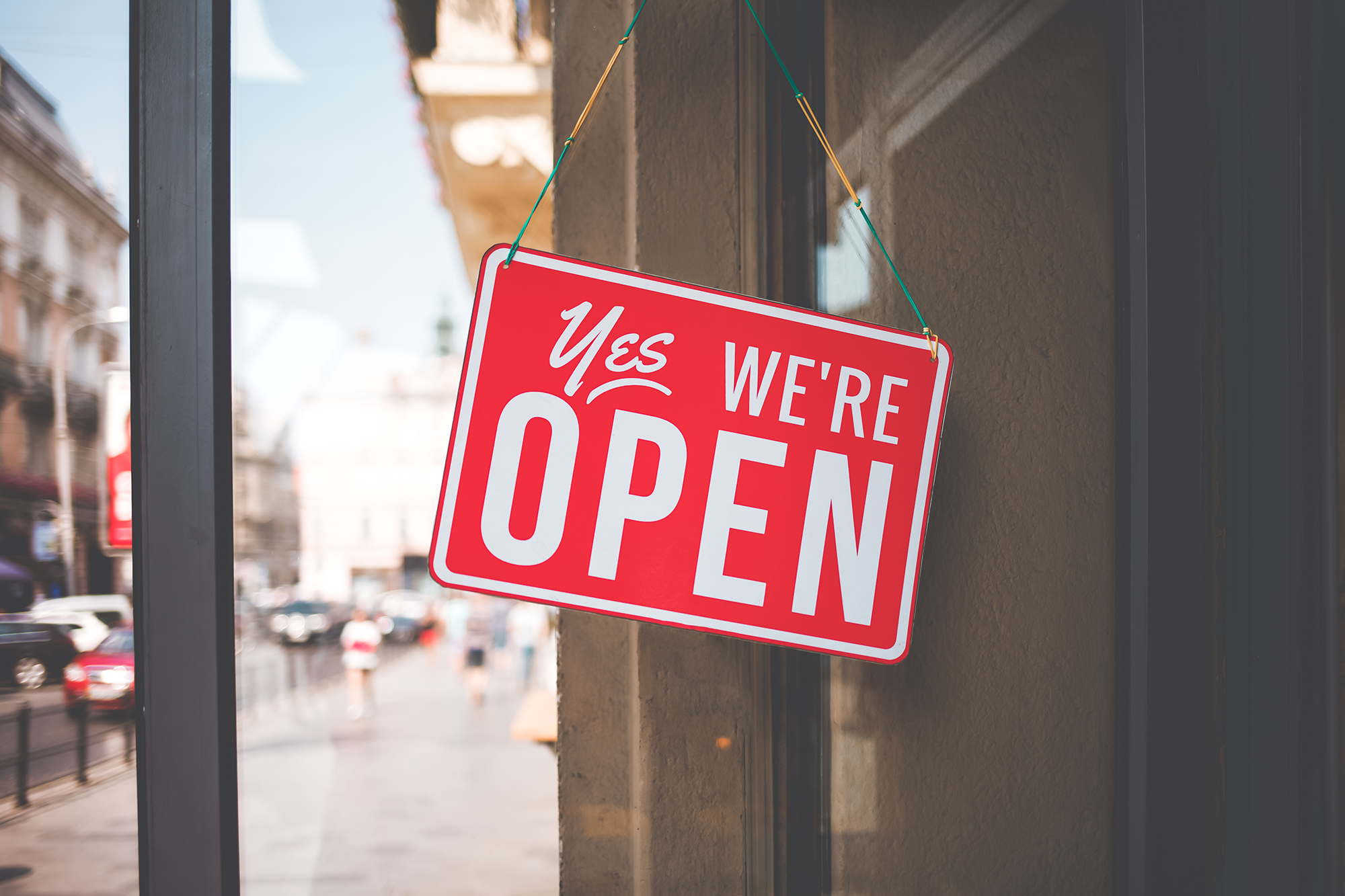 Yes we're open hanging storefront sign on small business door