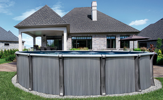 Above-ground swimming pool with gray panels in a landscaped backyard behind a modern brick house.