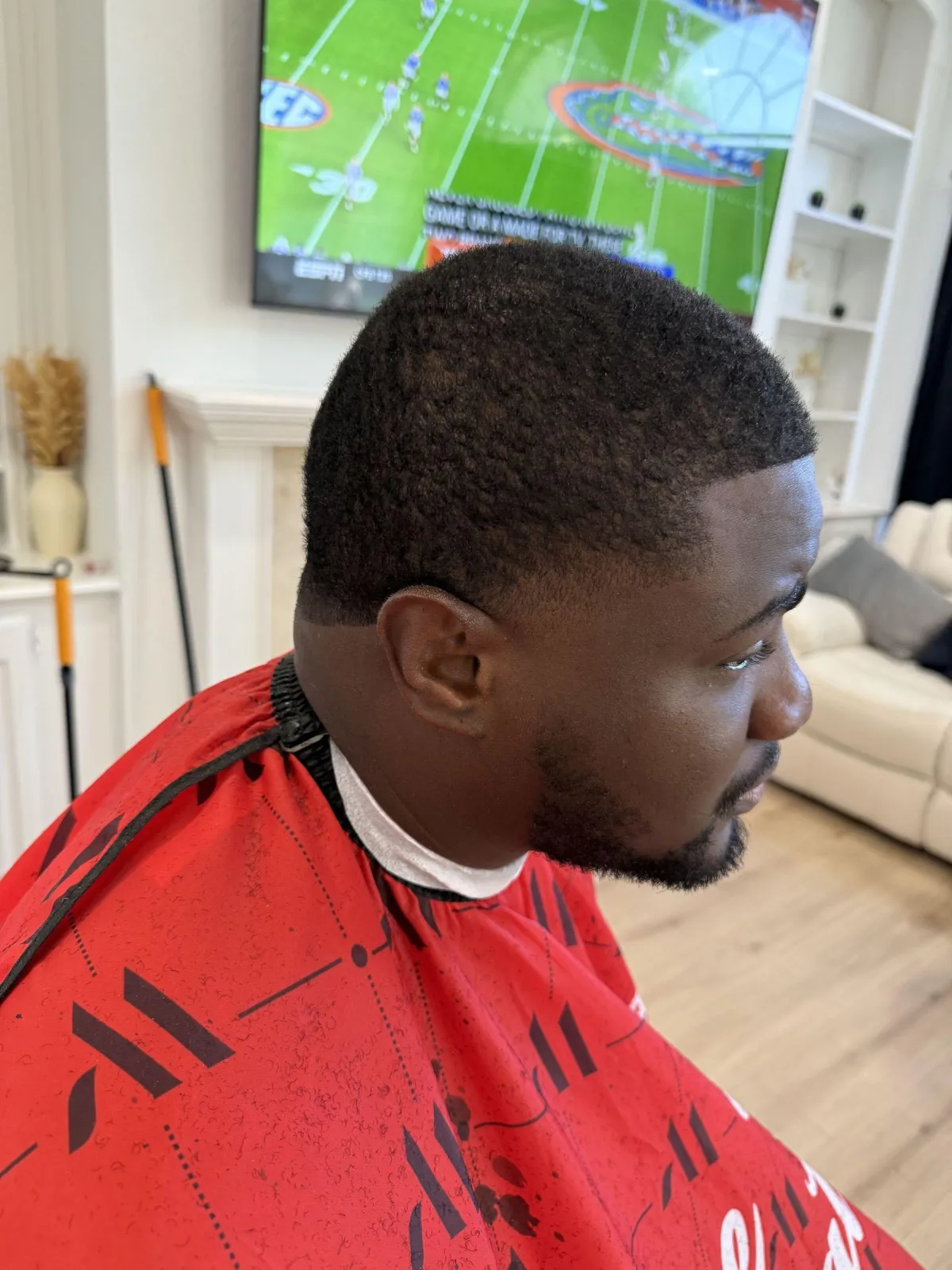 A skilled African American barber giving a clean fade to a female client with dark hair, detailed focus on clippers and blend, warm natural lighting, modern barbershop décor with shelves and mirrors softly blurred, professional grooming atmosphere.