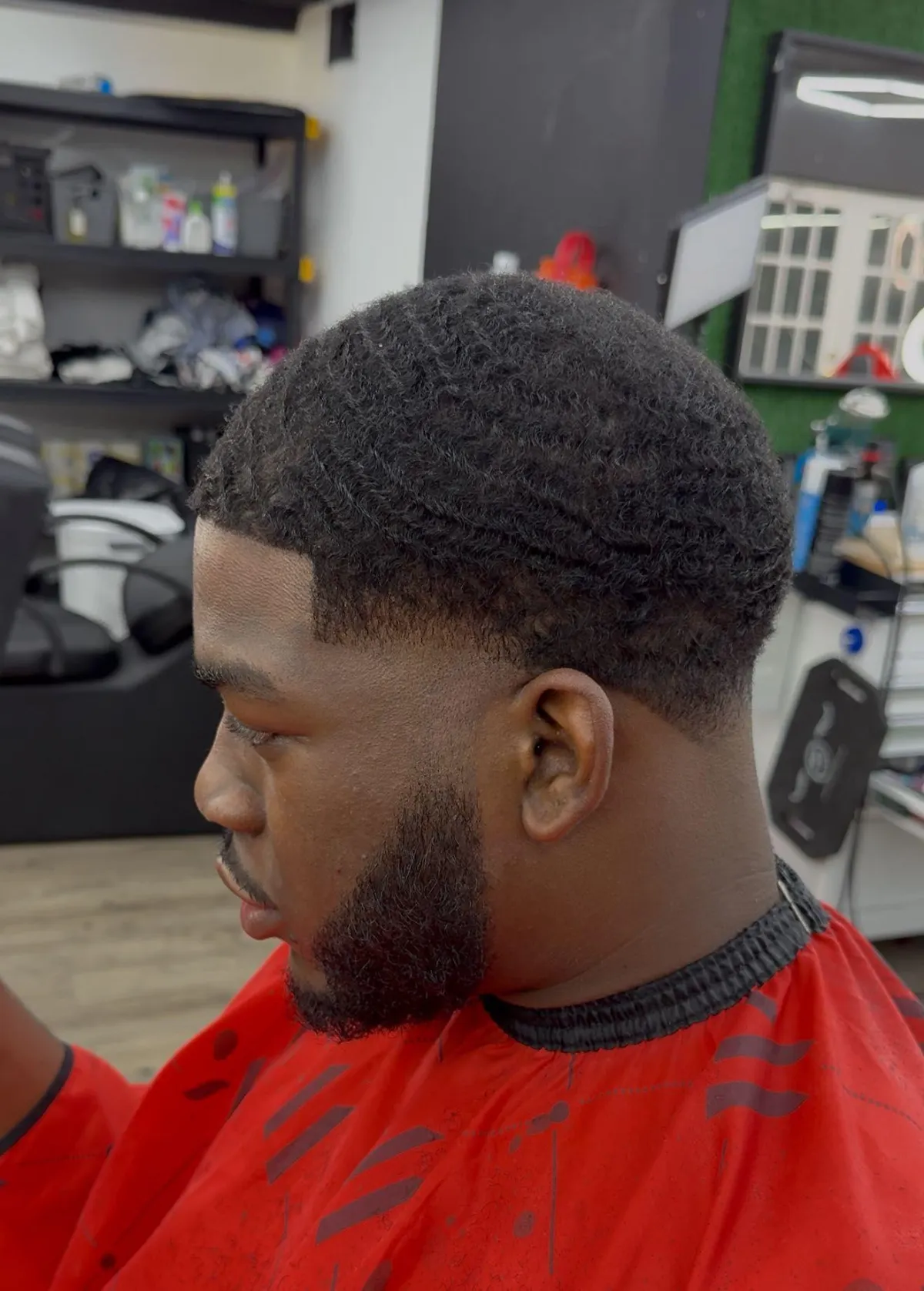 A skilled African American barber giving a clean fade to a female client with dark hair, detailed focus on clippers and blend, warm natural lighting, modern barbershop décor with shelves and mirrors softly blurred, professional grooming atmosphere.