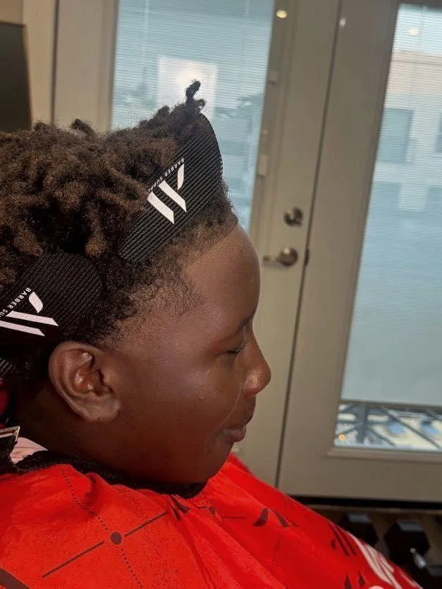 Barber tools on a workstation, including clippers, combs, grooming brushes, and an amber oil bottle, with a modern barbershop interior softly blurred in the background.
