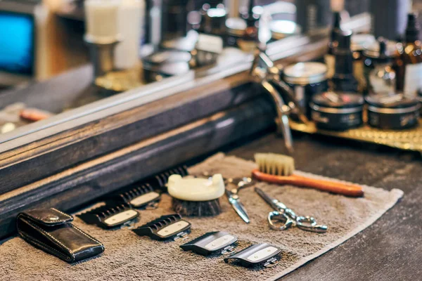 A widescreen hero image showing a clean set of barber tools—clippers, shears, a comb, brush, and straight razor—laid neatly on a counter. Background features a softly blurred modern barbershop interior with warm lighting. No text, no people, professional and sharp.