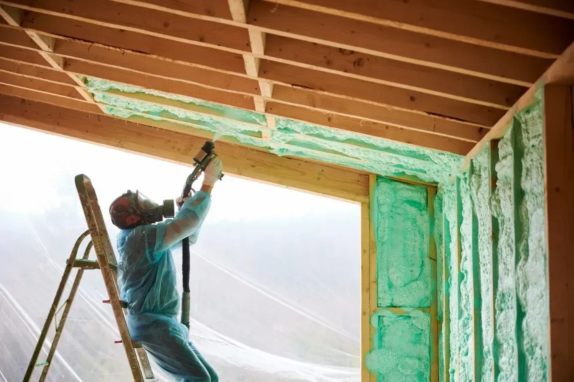 man spraying green spray foam insulation on the ceiling joists
