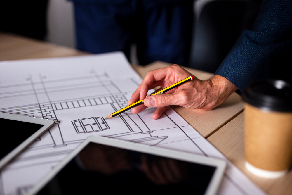 Contractor reviewing commercial interior design blueprints on desk with tablets and coffee.