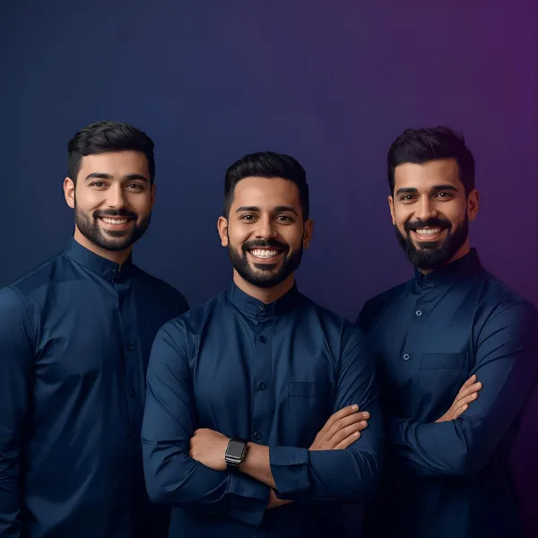 Portrait of three men standing together and smiling, all wearing matching dark blue traditional-style shirts against a softly lit background.