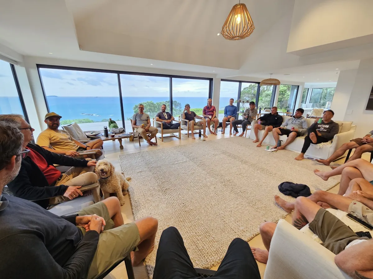 Men sitting in a circle during a MELD retreat session, ocean view behind