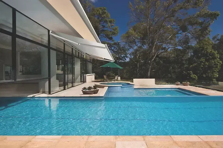 White retractable patio awning installed over a luxury glass-wall home with a swimming pool in Newport Beach, CA