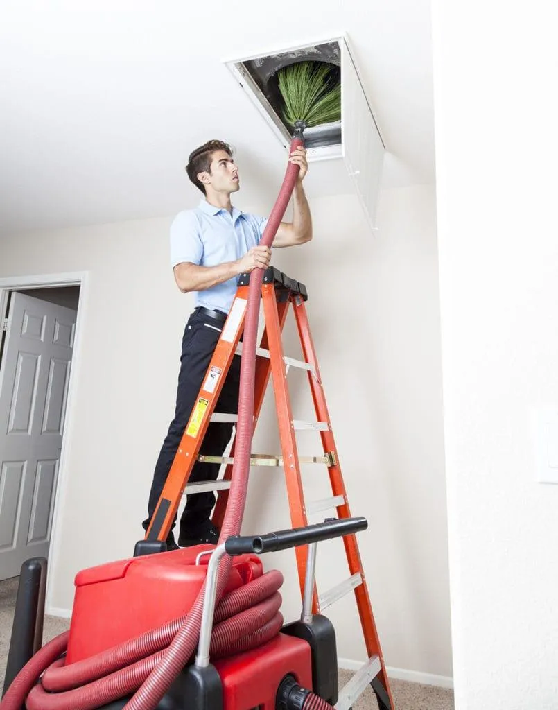 a person on a ladder cleaning a vent