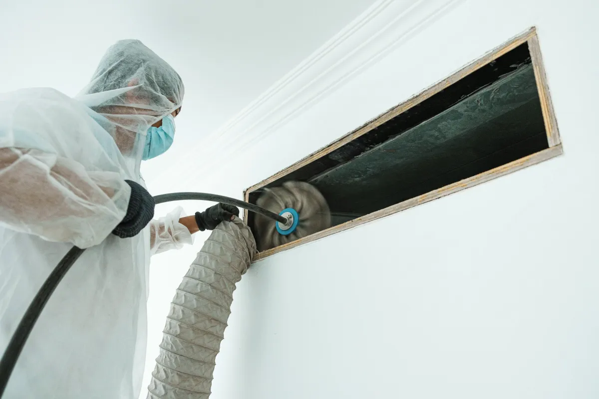 a person in a white suit using a machine to clean a duct