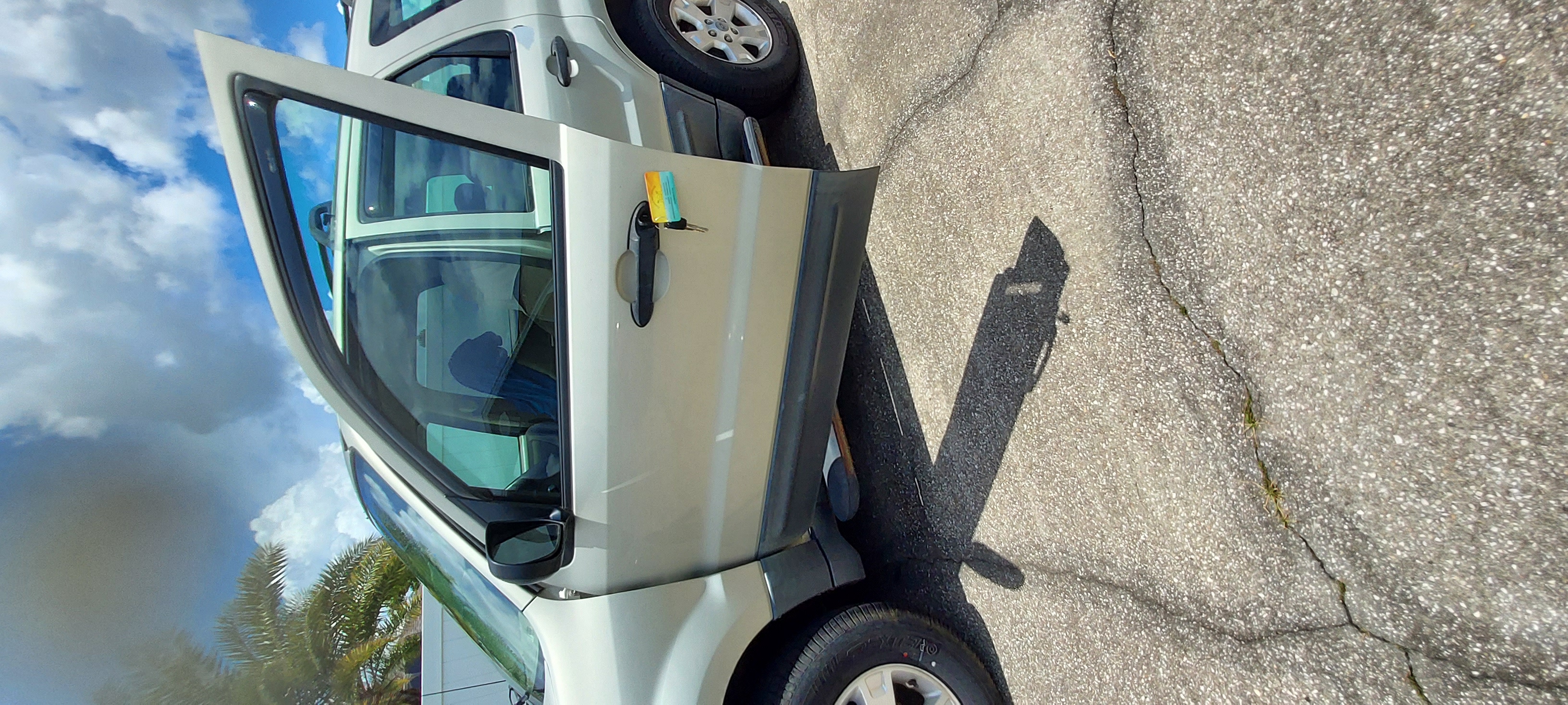 A locksmith in branded attire skillfully unlocking a sedan door in a busy parking lot, with focused expression and professional tools. The background shows city signage and parked cars, emphasizing urban expertise and quick response.