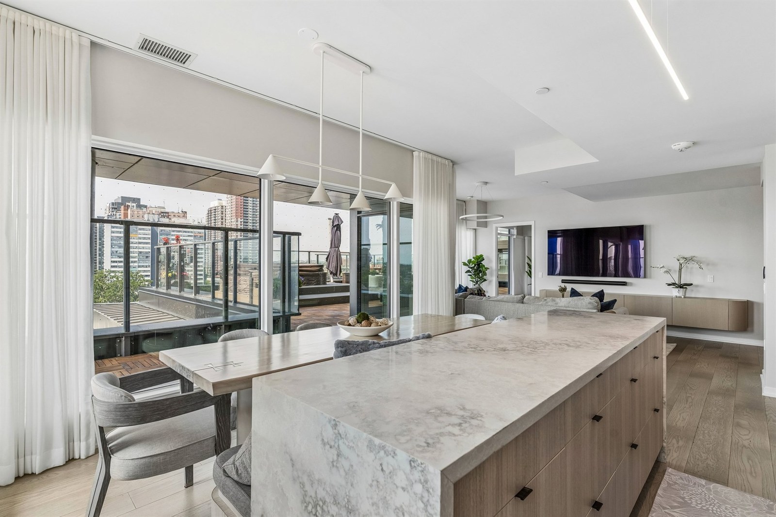 Open-concept luxury kitchen with marble island, custom fluted cabinetry, and floor-to-ceiling glass sliding doors opening to the terrace