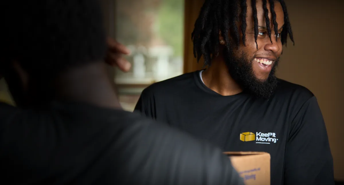 Smiling Keep It Moving Services crew member in a branded shirt, holding a box Smiling Keep It Moving Services crew member in a branded shirt, holding a box