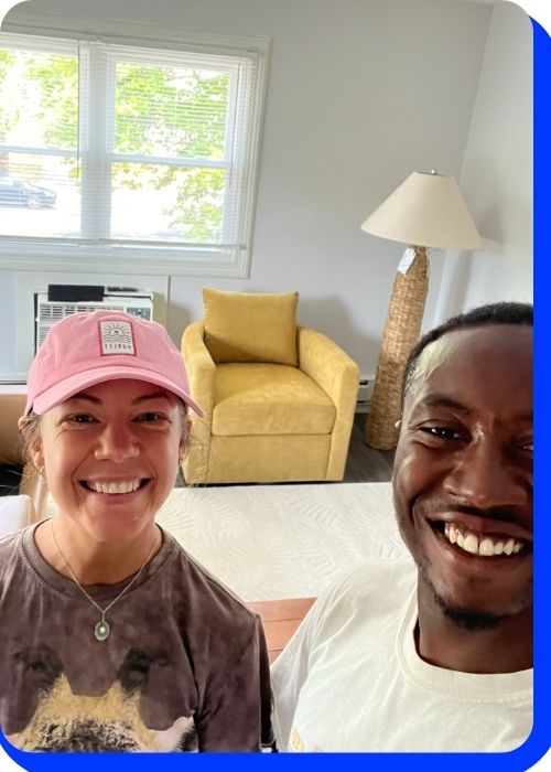 Smiling woman in a pink cap and man in a white shirt posing in a bright living room with a yellow chair and a lamp, reflecting the friendly service of Keep It Moving Services NJ.