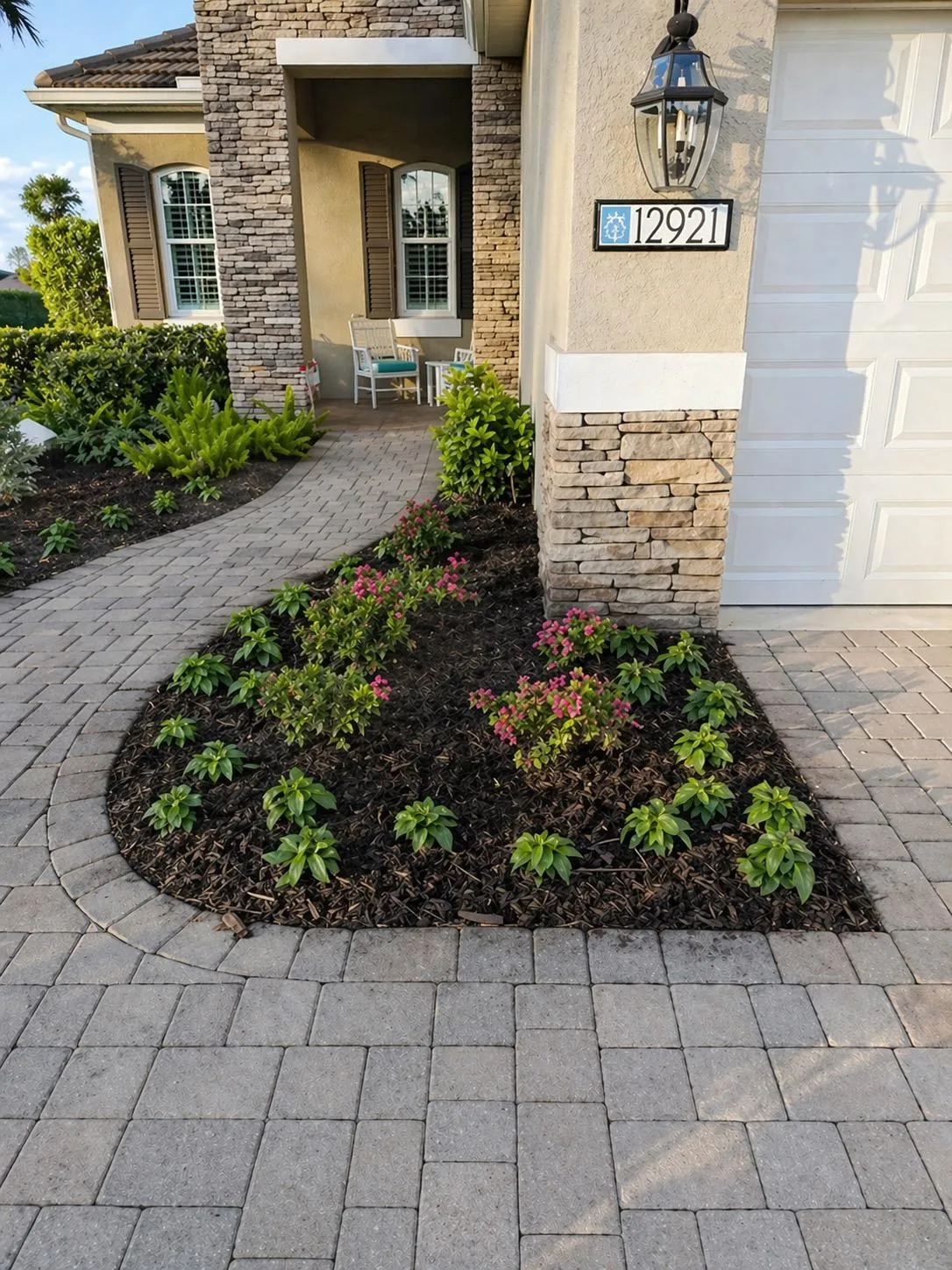 Front yard landscape enhancement with colorful plants, fresh mulch, and paver driveway at a residential home