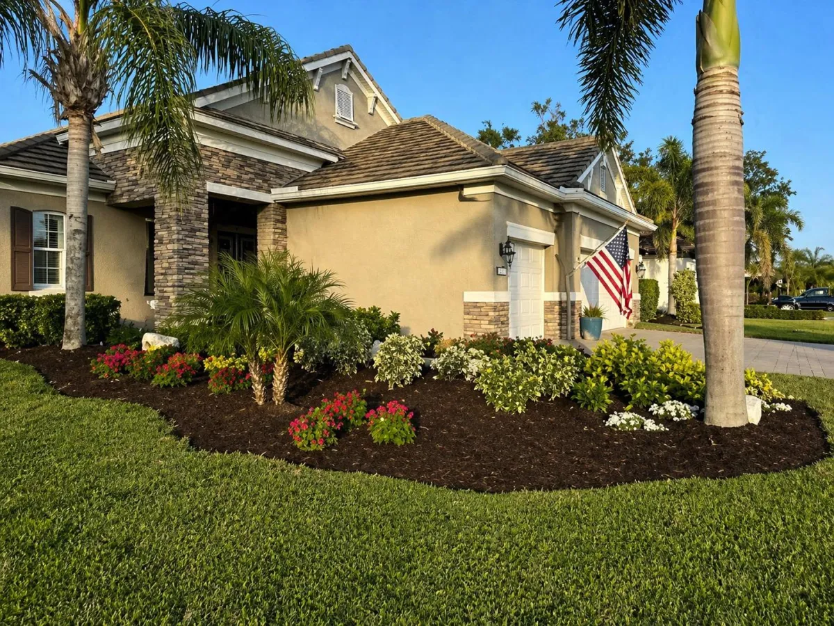 Front yard landscape installation with colorful flowering plants, palm trees, and fresh mulch beds improving residential curb appeal