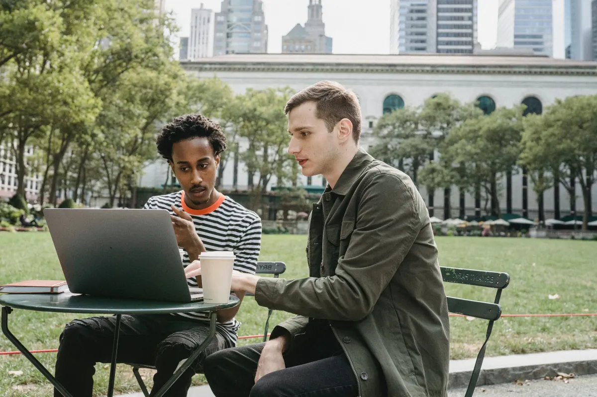 Two people in a park with a laptop on a small circular metal table.