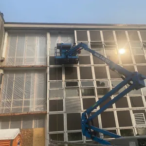 Worker on a lift outside of a building removing windows and placing plastic over removed openings.