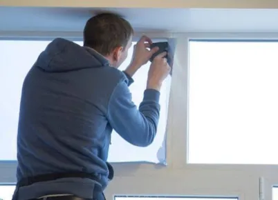 Worker on a lift outside of a building removing windows and placing plastic over removed openings.