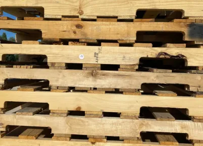 Two large trucks angled from he rear, each with a very large load of hundreds of wooden pallets.