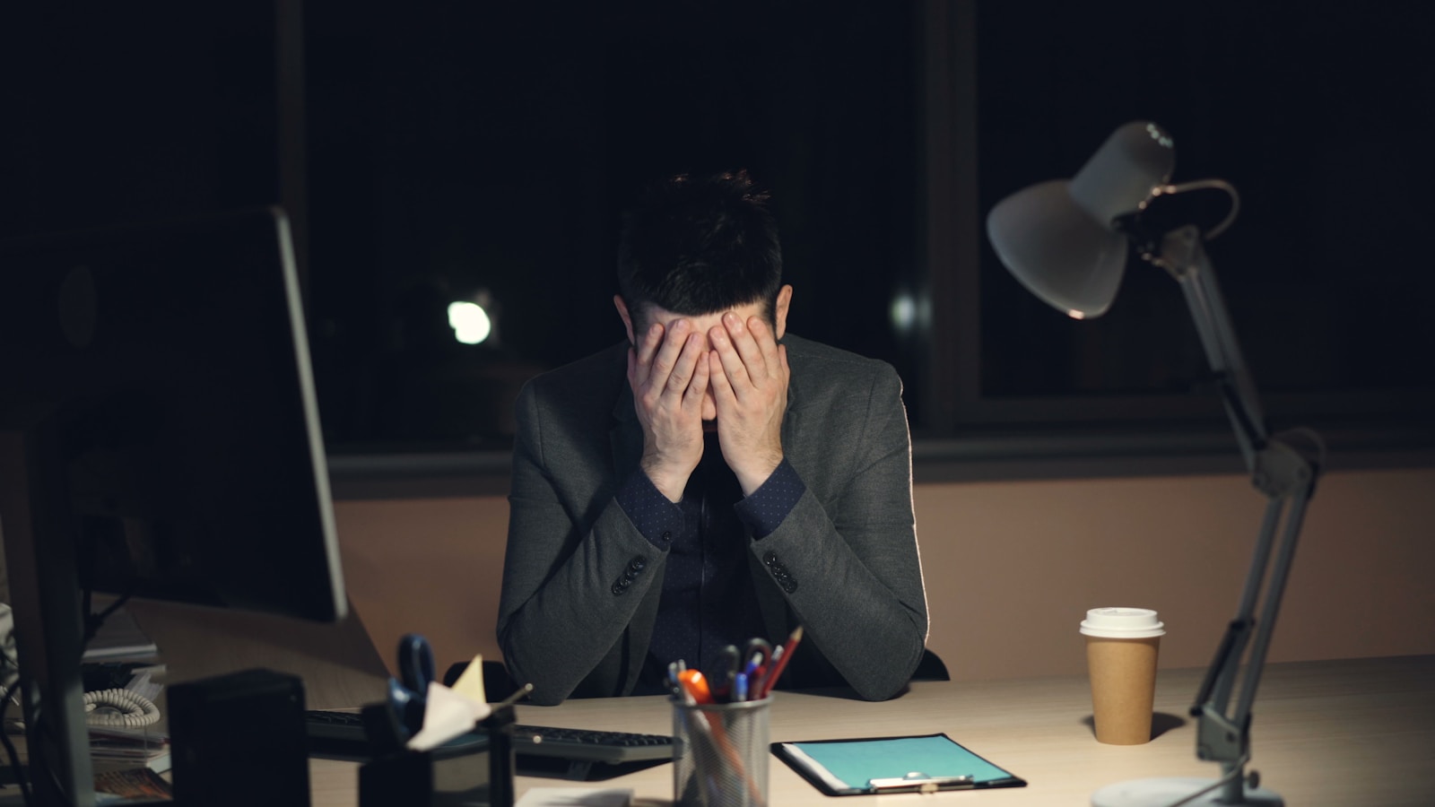 Trader sitting alone at a dark desk with his head in his hands after a losing session