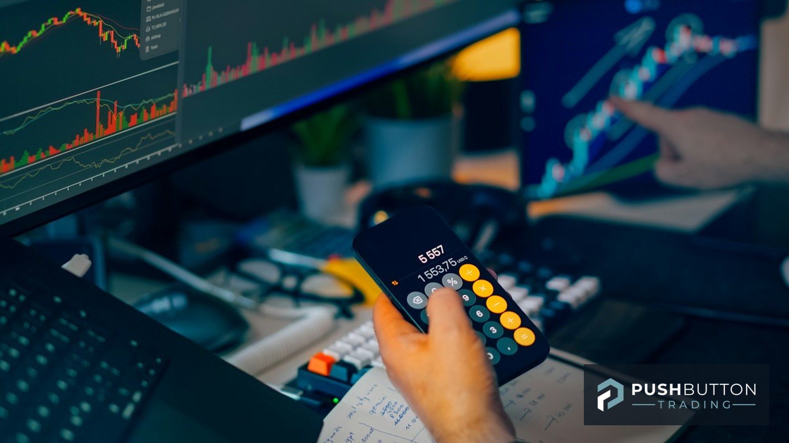 Trader using a calculator to size a position while reviewing candlestick charts on multiple monitors