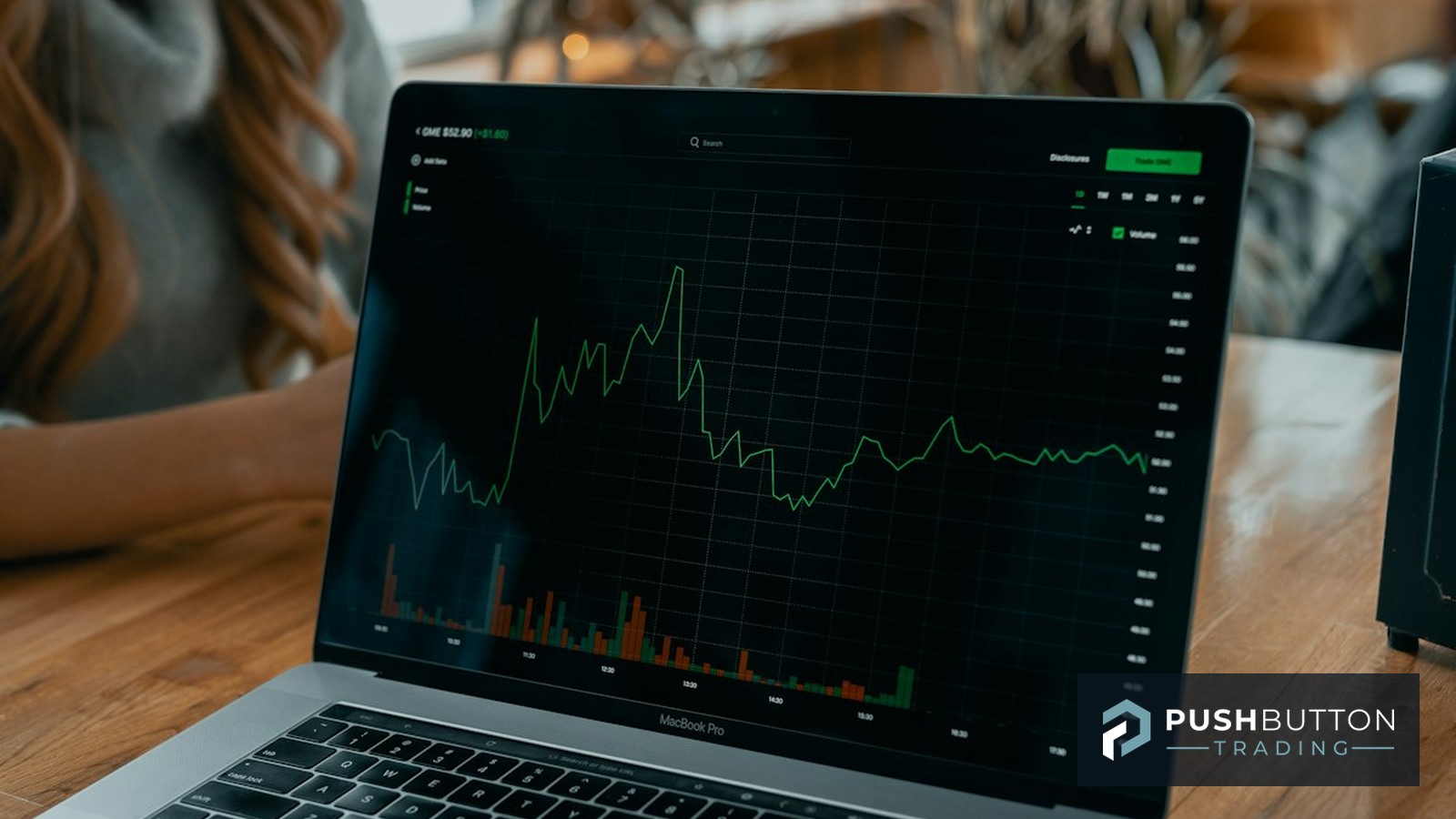 Laptop showing a stock price chart on a wooden desk, Push Button Trading logo overlay