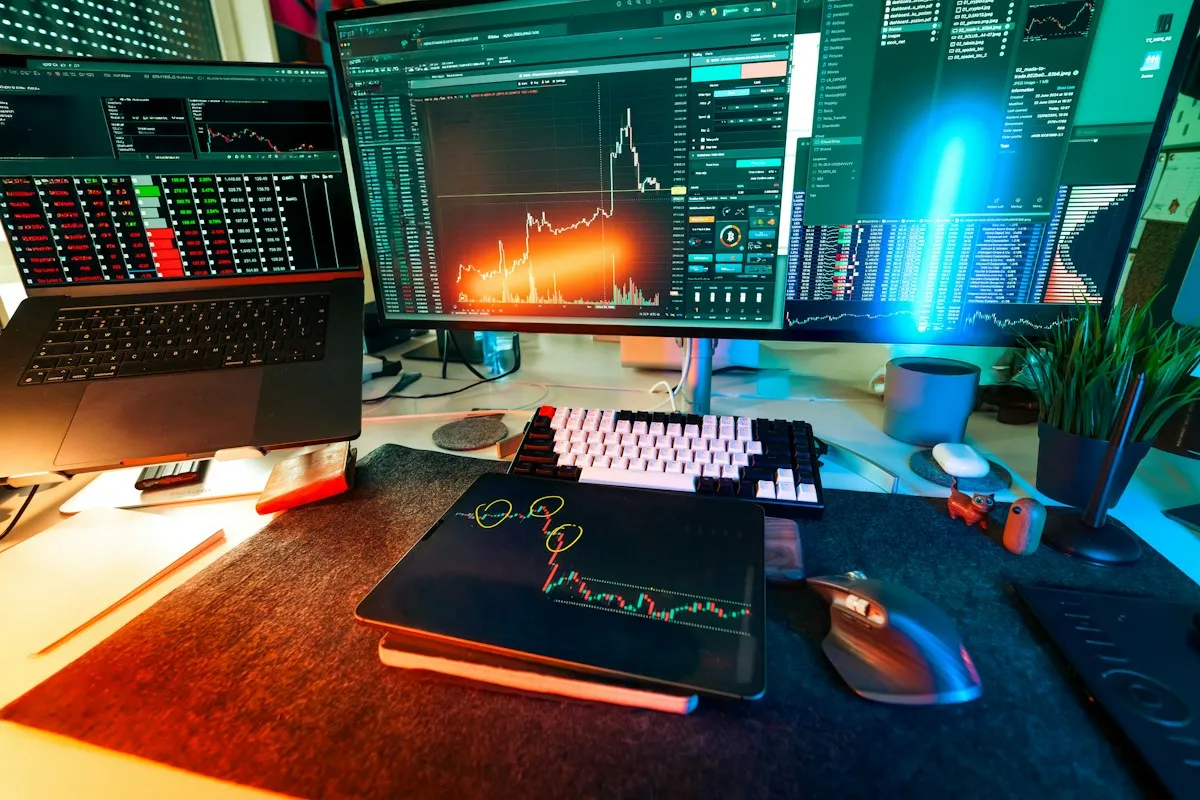 Multi-monitor trading desk with a laptop, candlestick chart display, and a tablet showing an annotated chart marking entry signals, representing multiple automated accounts running at once