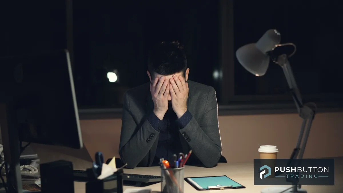Trader sitting alone at a dark desk with his head in his hands after a losing session