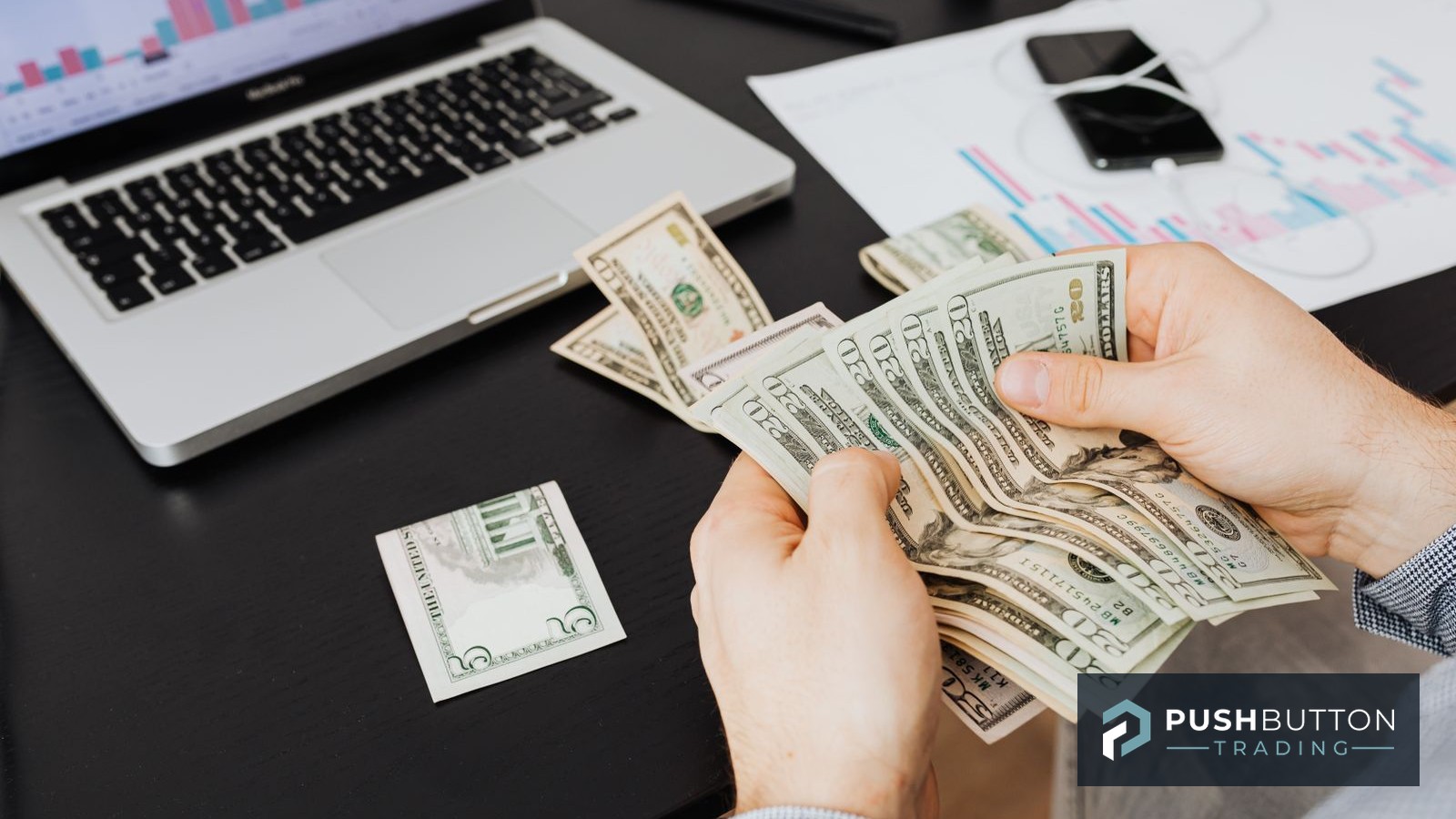 Trader counting cash at a desk beside a laptop showing performance charts