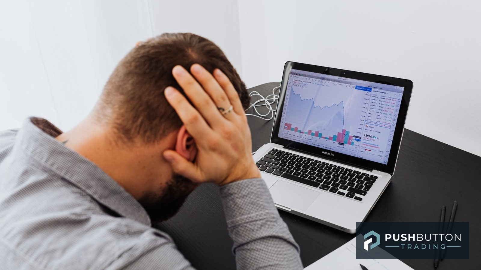 Futures trader with his head in his hands in front of a laptop showing a declining market chart