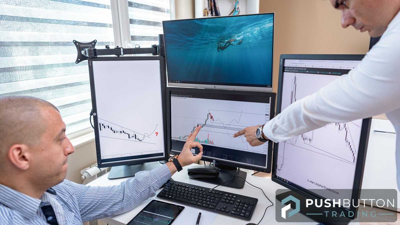 Two traders reviewing candlestick charts across a multi-monitor trading desk