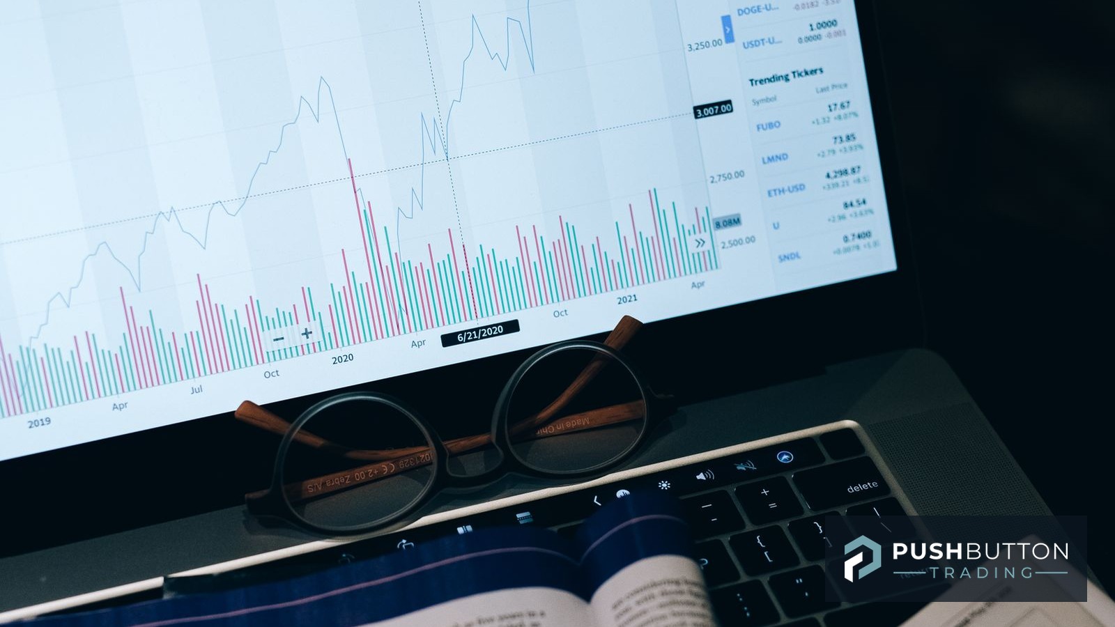 Laptop showing a market chart with reading glasses resting on the keyboard beside notes